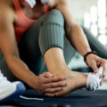 Kobieta na siłowni trzyma się za bolącą stopę. Co to jest ganglion w stopie