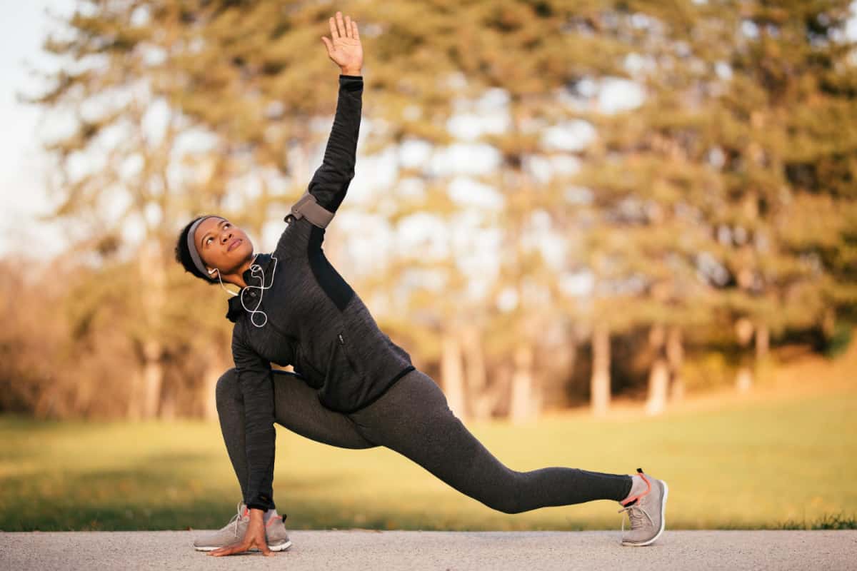 Kobieta rozgrzewa się przed bieganiem w parku - Stretching dynamiczny - proste ćwczenia