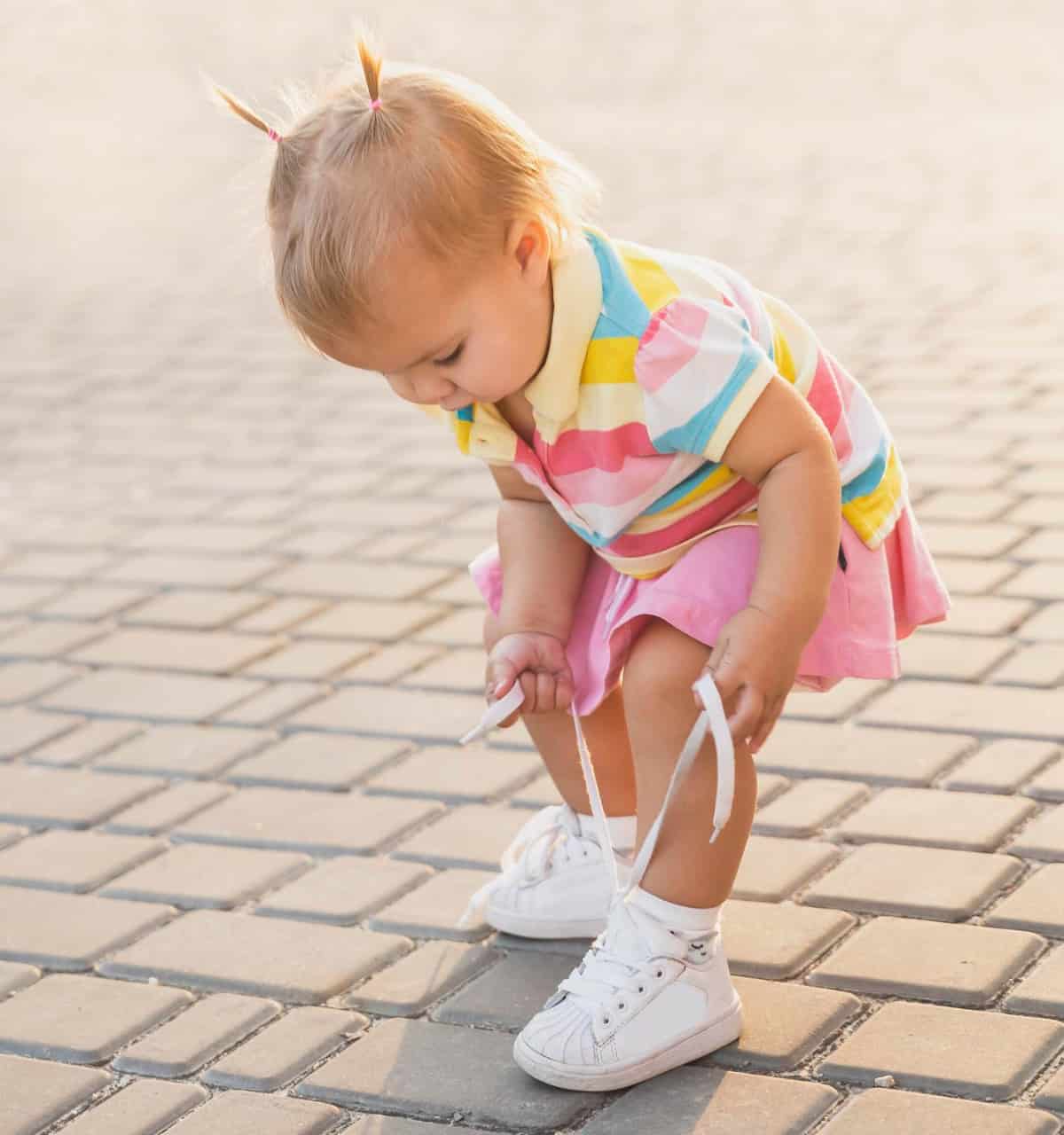 Dziewczynka ciągnie za sznurówki swoich butów. Płaskostopie u dzieci