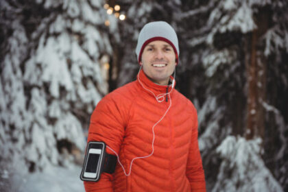 Mężczyzna z telefonem na ramieniu biega zimą przez las - Bezpieczne bieganie zimą — co zrobić, by takie było